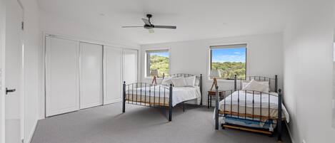 A bedroom with two beds, a ceiling fan, and large windows with a view of greenery.