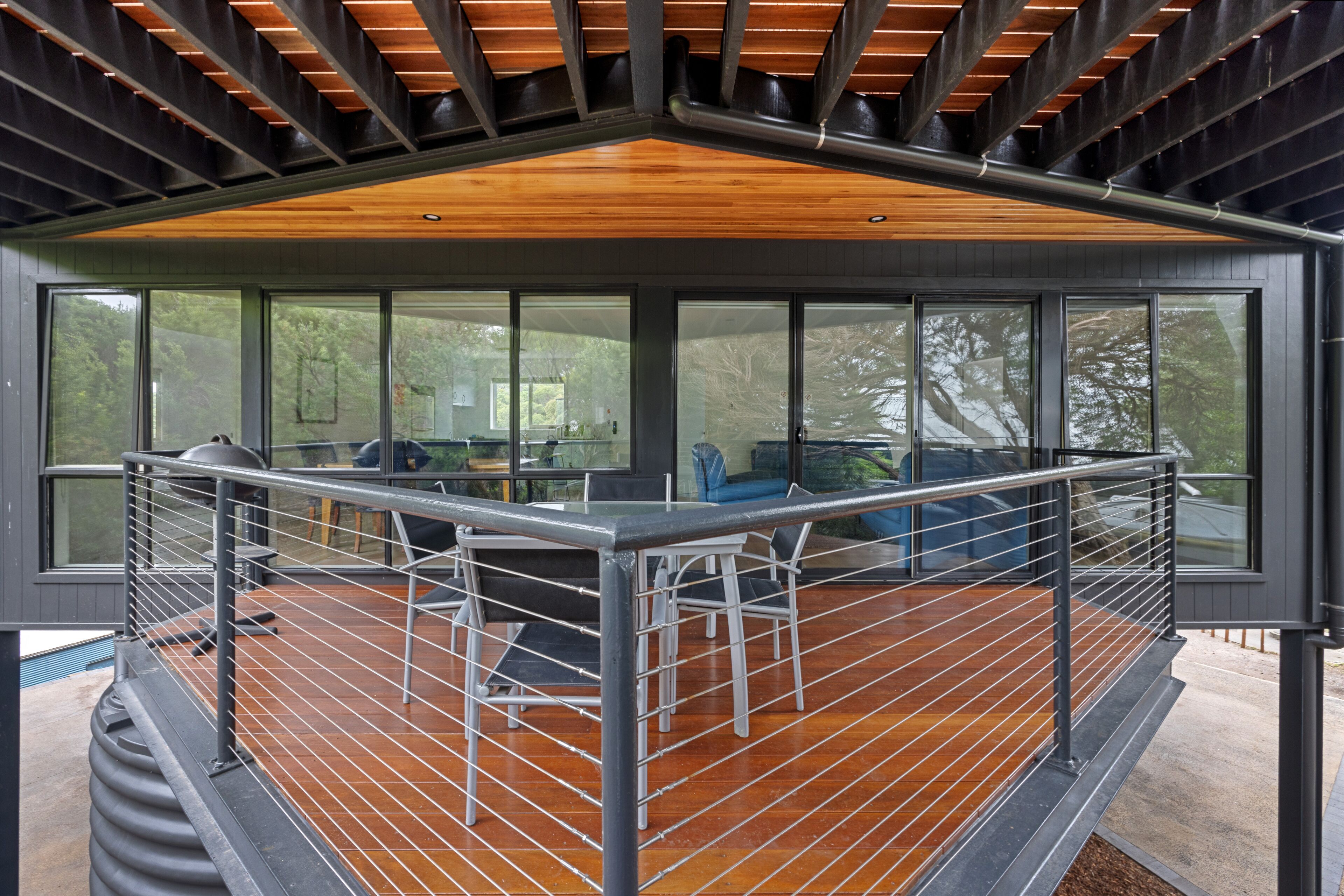Une terrasse extérieure moderne, dotée d’un plancher en bois et d’une rambarde en métal, qui offre une vue sur une zone boisée.