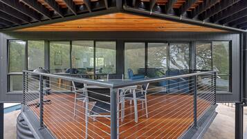 Une terrasse extérieure moderne, dotée d’un plancher en bois et d’une rambarde en métal, qui offre une vue sur une zone boisée.