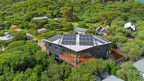 Una casa moderna con paneles solares, rodeada de vegetación exuberante y con vista despejada al océano.
