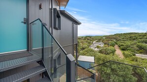 Un edificio moderno con una escalera de cristal que conduce a un balcón, con vistas a un paisaje exuberante y verde.