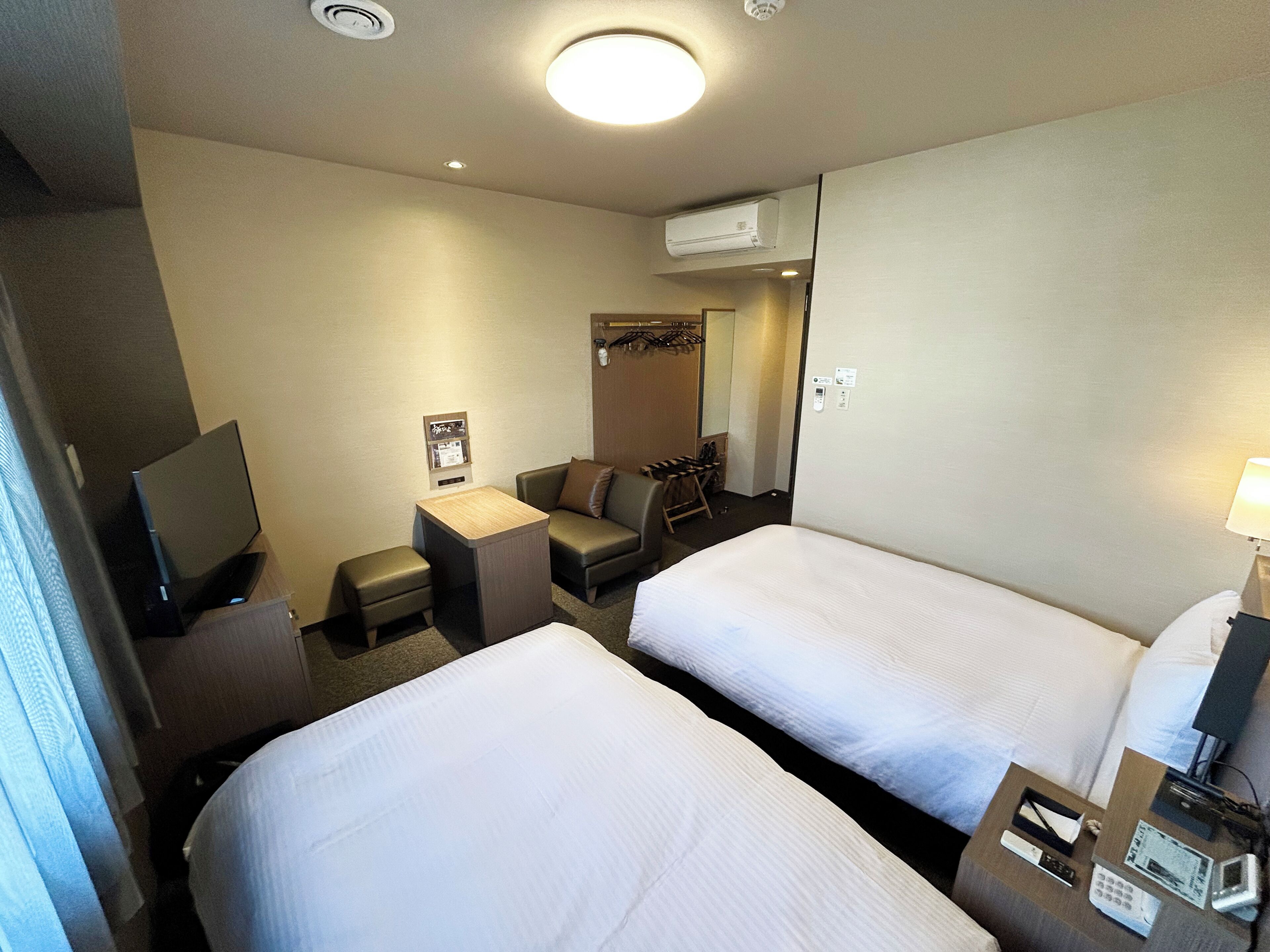 Ein Hotelzimmer mit zwei Betten, einem Schreibtisch, einem Stuhl, einem Fernseher und einem Spiegel.