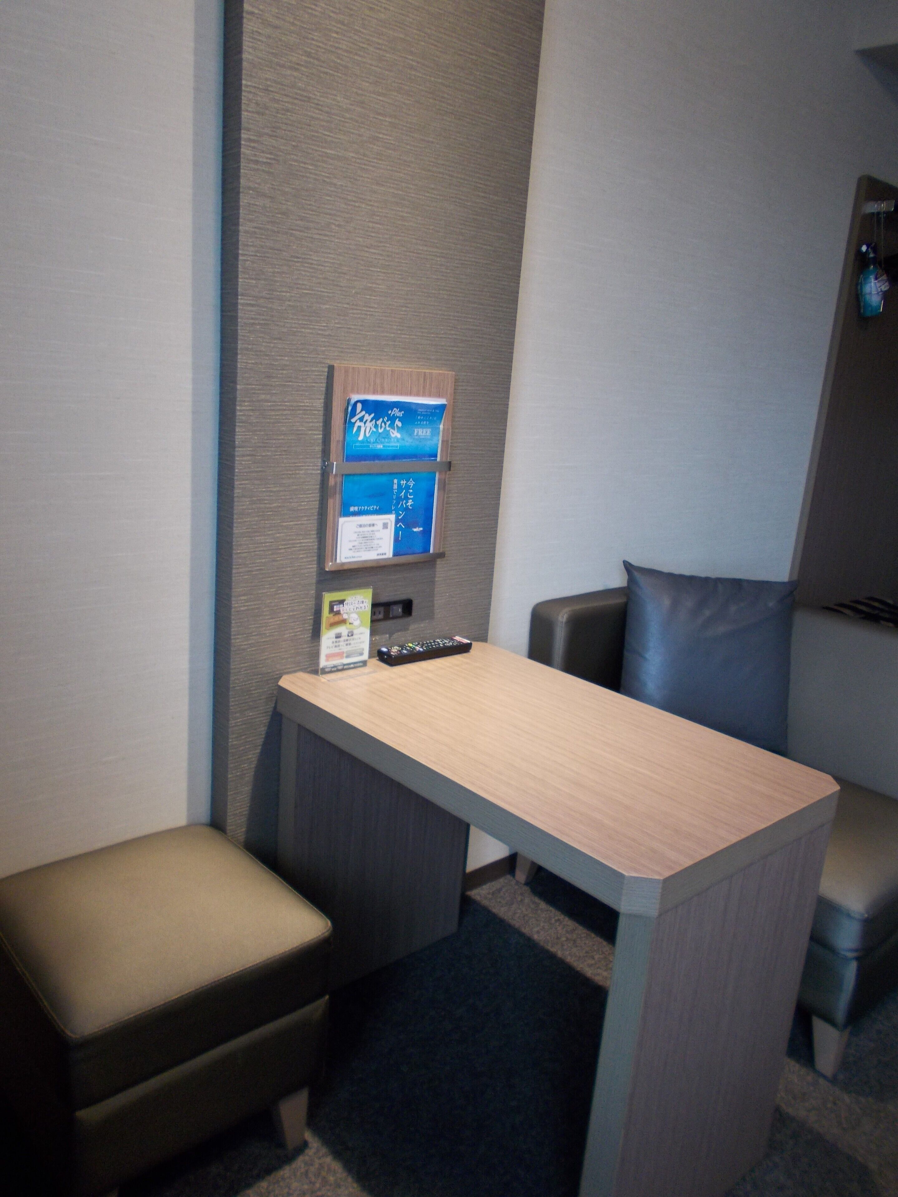 A small office space with a desk, two chairs, a vending machine, and a remote control on the desk.