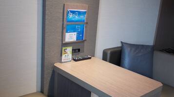 A small office space with a desk, two chairs, a vending machine, and a remote control on the desk.