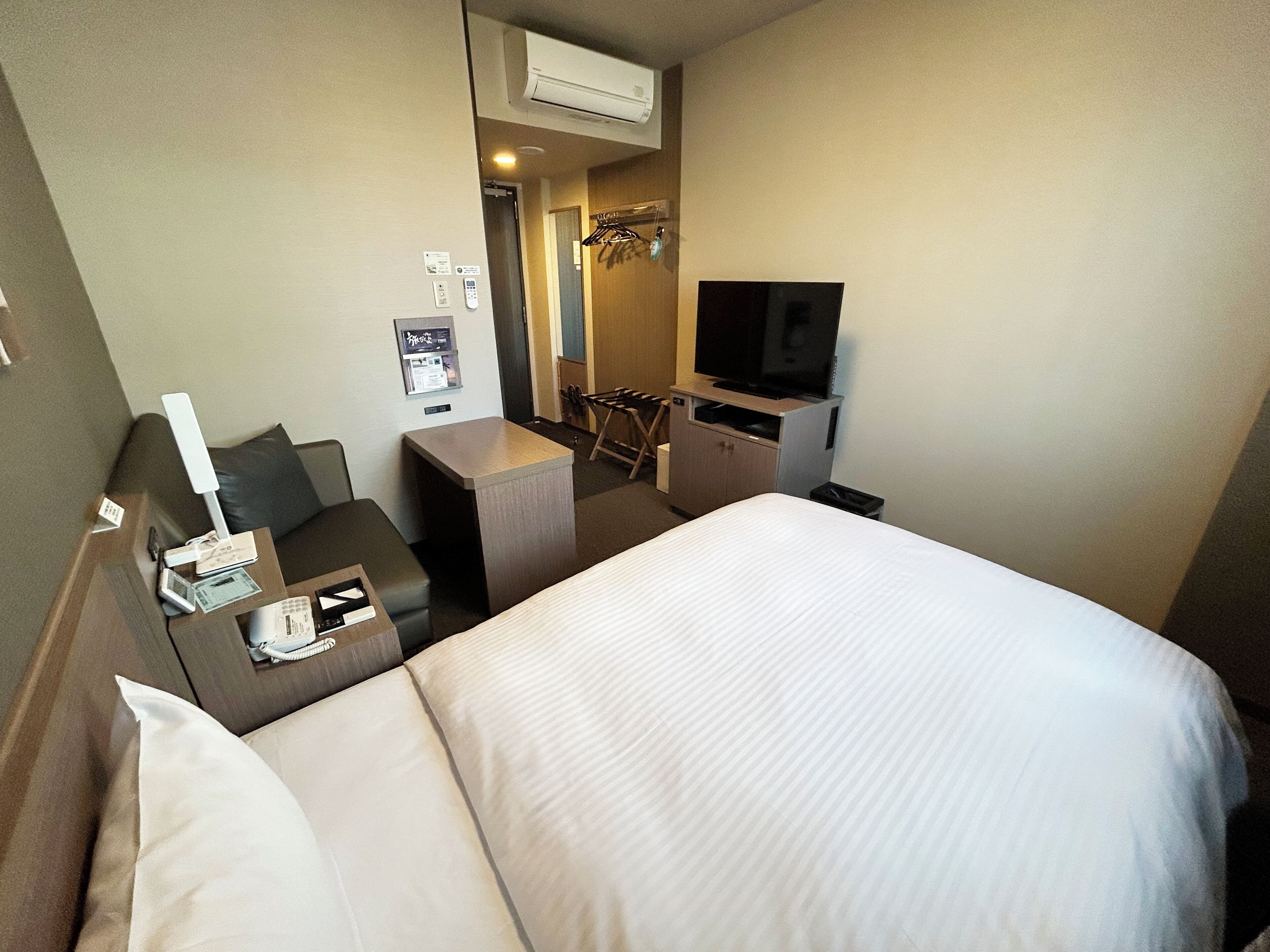 A hotel room with a bed, a desk, a television, and a mirror.