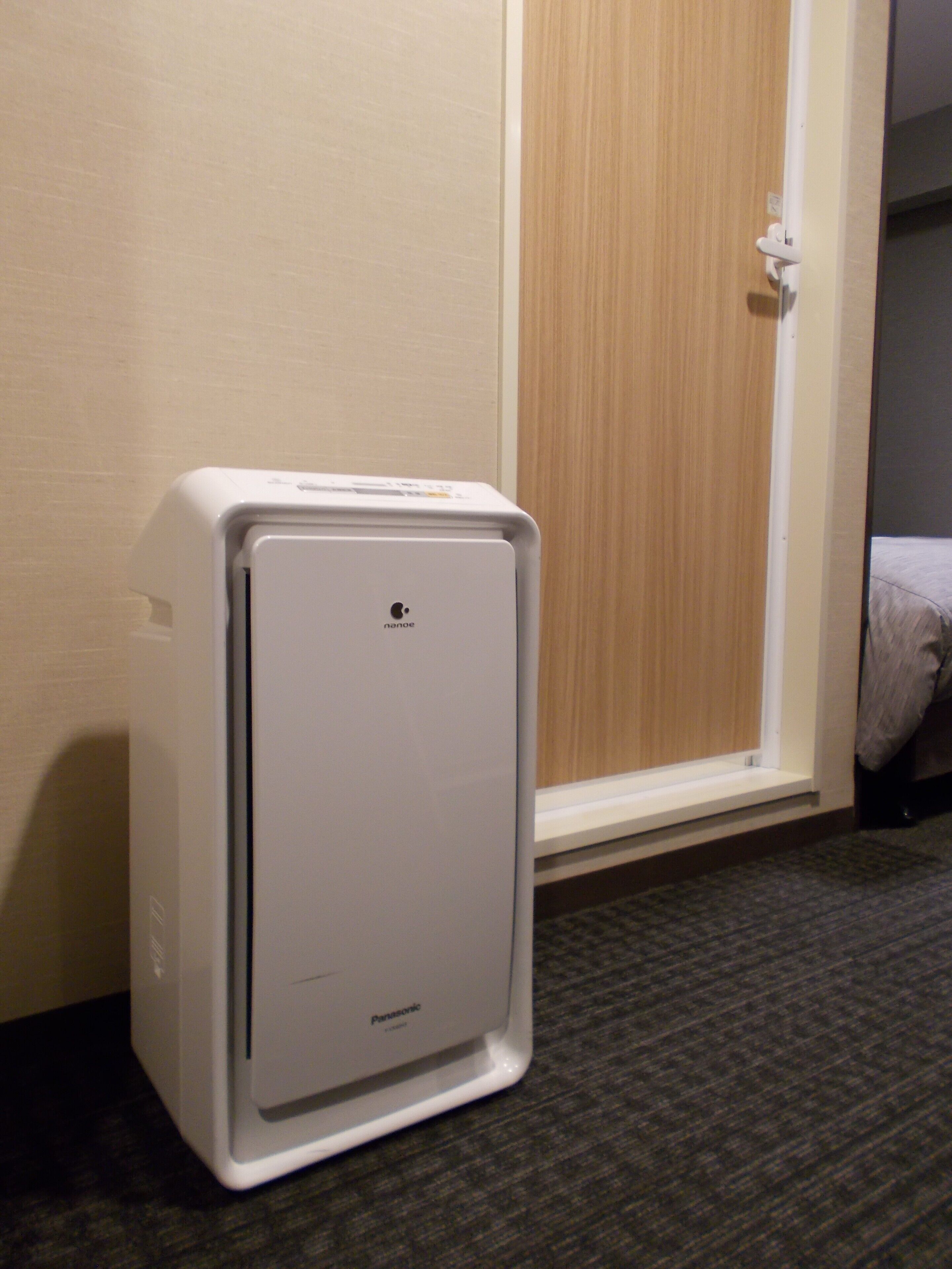 A compact, white portable heater in a hotel room with a wooden door and a carpeted floor.