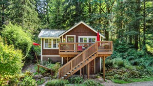 A wooden cabin with a balcony and stairs, surrounded by dense forest.