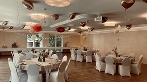 Un amplio salón de banquetes con mesas redondas, sillas blancas y globos con forma de corazón.