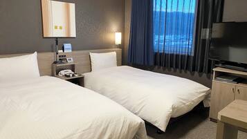 A hotel room with two beds, a desk, a TV, and a window with curtains.