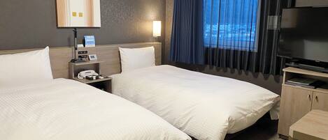 A hotel room with two beds, a desk, a TV, and a window with curtains.