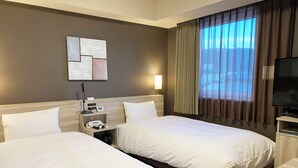 Une chambre d’hôtel avec deux lits, une télévision, un bureau, une lampe et une fenêtre avec des rideaux.