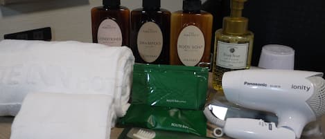 Toiletries including shampoo, body soap, and a hair dryer on a hotel counter.