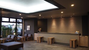 Un espace d’accueil au design moderne, comprenant un comptoir de réception, un coin salon avec des fauteuils et des poufs, et un mur orné de motifs.