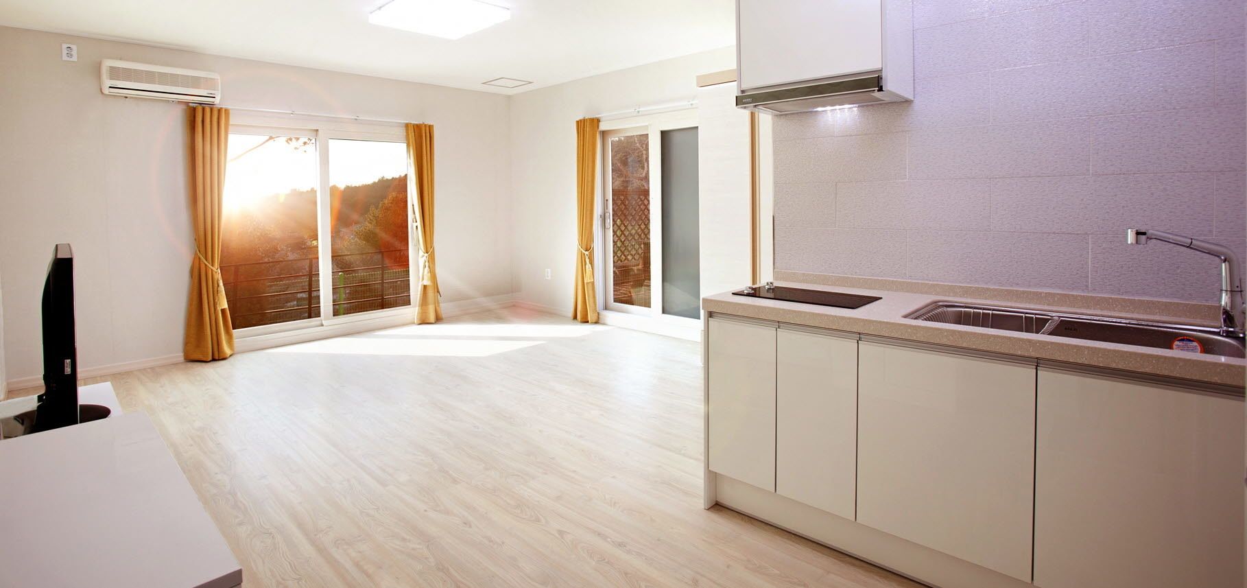 A modern kitchen with a built-in dishwasher, a large window with curtains, and a view of a balcony.