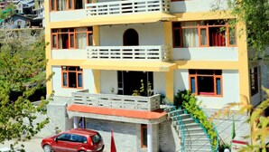 A multi-story hotel with balconies, a red car parked in front, and a mountainous backdrop. - Zarim Hotel Manali (Manali)