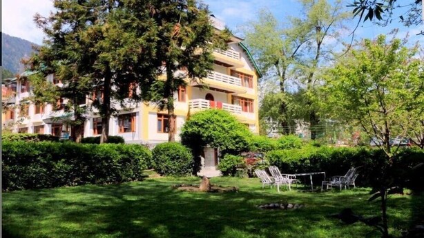 A multi-story building with balconies, surrounded by lush greenery and a well-maintained lawn. - Zarim Hotel Manali (Manali)