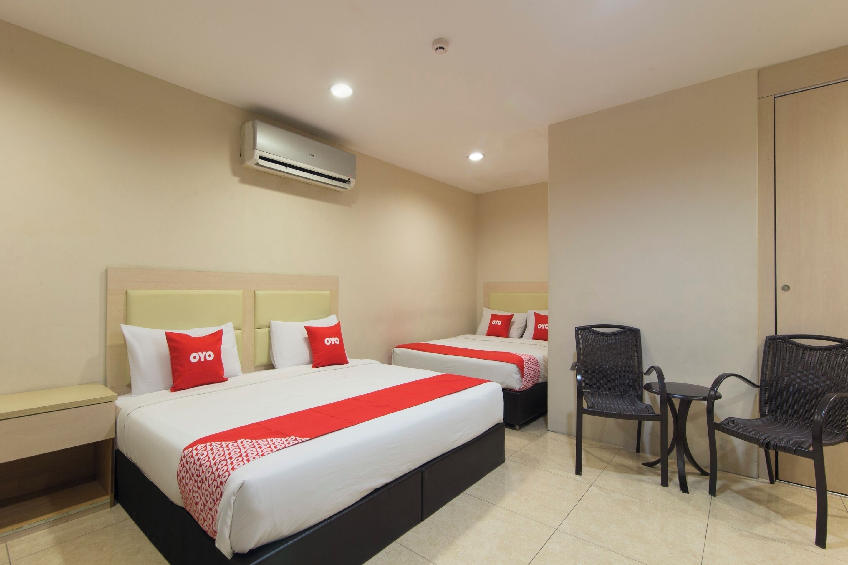 Habitación de hotel con dos camas, una mesita, dos sillas, una mesita de noche y un equipo de aire acondicionado.