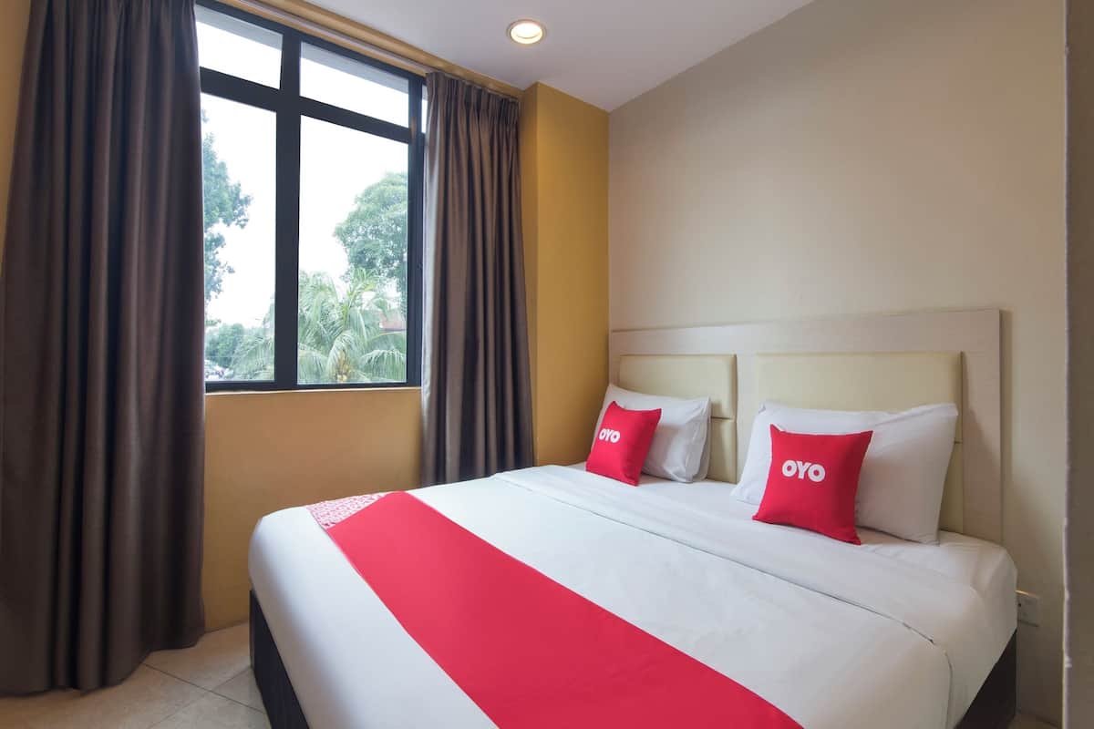 Une chambre d’hôtel avec un grand lit, deux oreillers portant la marque « OYO », une fenêtre avec des rideaux et une vue sur la verdure environnante.