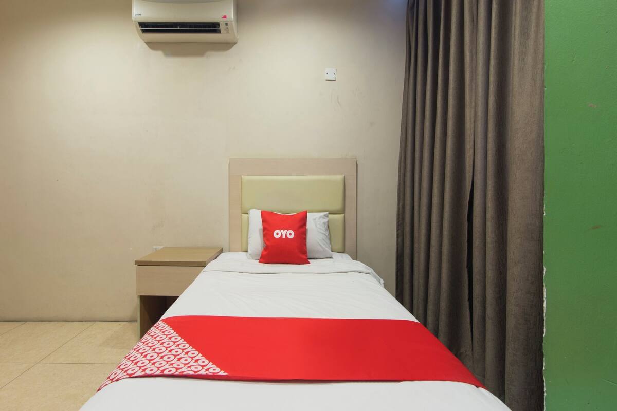 Une chambre d’hôtel avec un lit, une table de chevet, un climatiseur fixé au mur et un mur peint en vert.