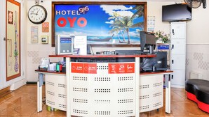 Un comptoir d’accueil d’hôtel avec une horloge, un téléviseur, un ordinateur et un panneau indiquant les heures d’arrivée et de départ.