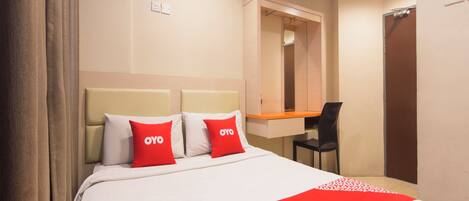 A hotel room with a bed, two red pillows, a desk, and a mirror.