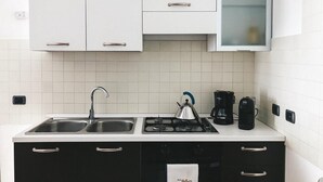 Ett kök med vita skåp, en dubbeldiskho, en gasspis, en vattenkokare, en kaffebryggare och en mikrovågsugn.