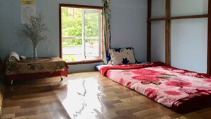 Una stanza con pavimento in legno, un letto con copriletto floreale, un tavolino con un vaso e una finestra vista verde.