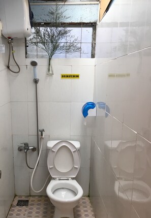 A small, tiled bathroom with a toilet, shower, and a window with a view of trees. - Dalat Chocolate Homestay (Cam Ly - Da Lat)