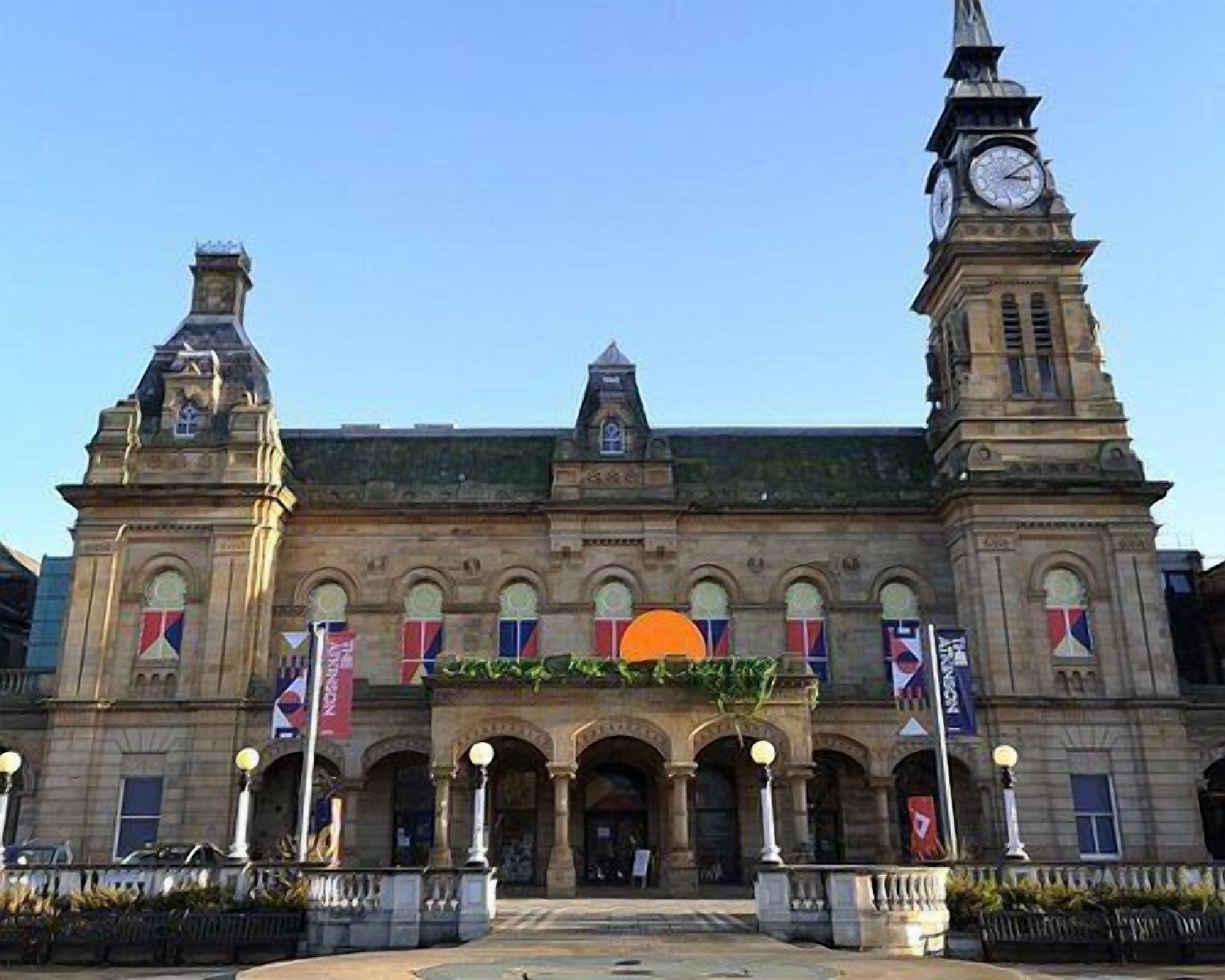A historic building with a central archway, two clock towers, and multiple flags.