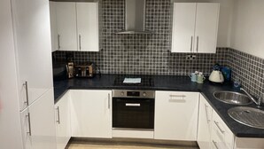 A modern kitchen with white cabinets, a black countertop, a built-in oven, and a stainless steel sink. - Beach House Courtyard 1 bed (Southport)