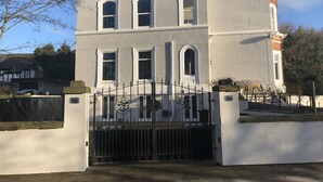 A two-story building with a symmetrical facade, a gated entrance, and a small tower-like structure on the right. - Beach House Courtyard 1 bed (Southport)