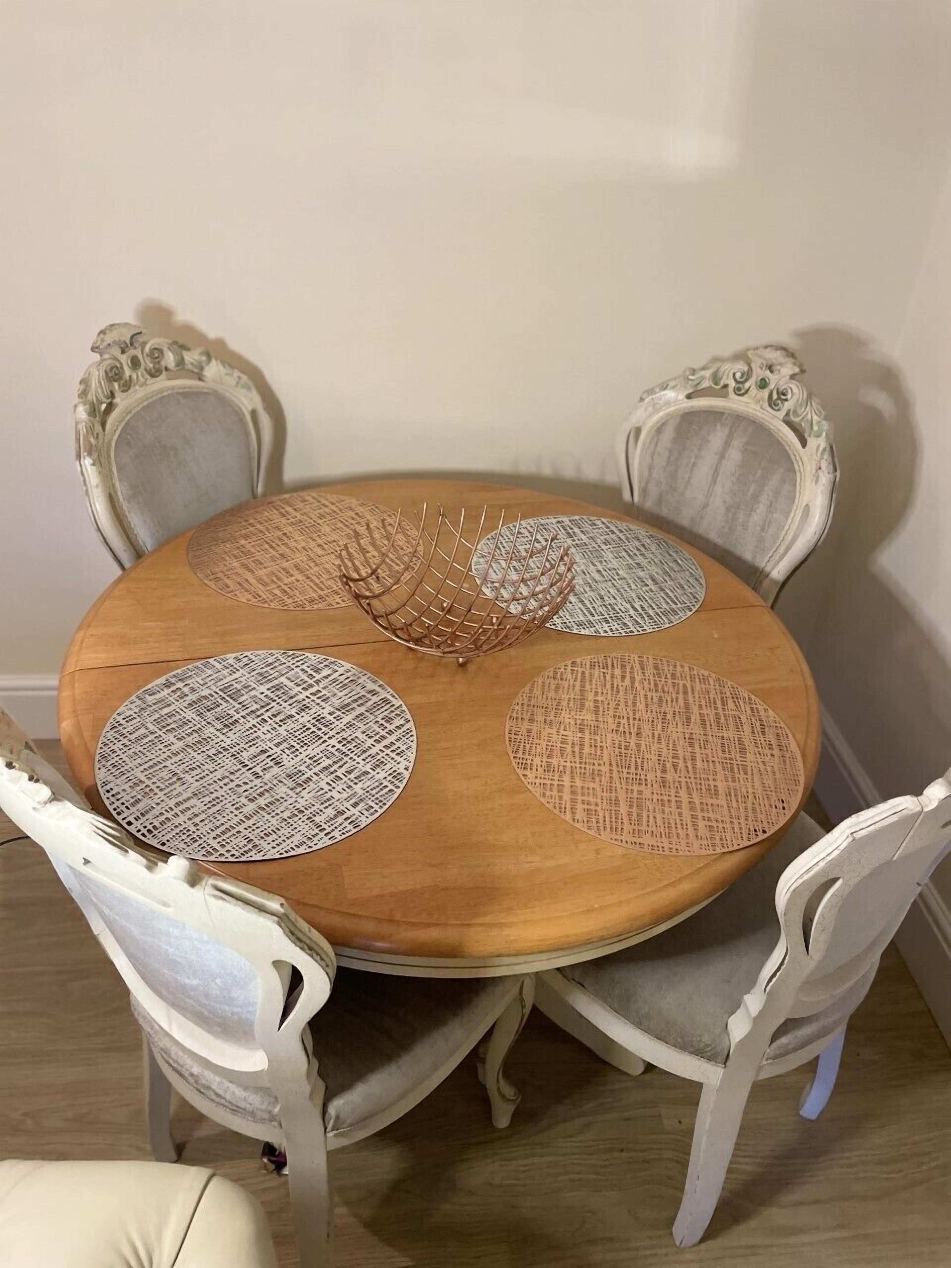 A round wooden dining table with four chairs, each with a cushioned seat and a decorative backrest.