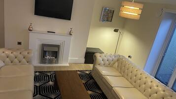 A living room with a fireplace, a sofa, a coffee table, and a TV mounted on the wall.