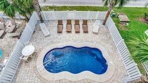 Ein Pool mit gewelltem Rand, umgeben von einem weißen Zaun, mit Liegestühlen und einem Tisch ausgestattet.