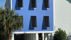 Ein zweistöckiges Gebäude mit blauer Fassade und weißen Verzierungen, inklusive überdachter Eingangspartei und sichtbarer Hausnummer.