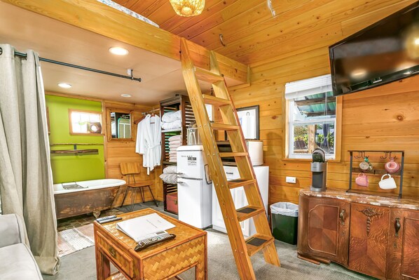 L’intérieur d’une cabane en bois, avec une échelle en bois, un réfrigérateur, un évier, une table avec une télécommande et un placard.