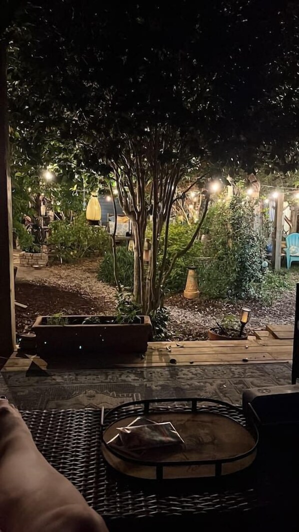 Ein Patio mit Tisch und Stühlen, umgeben von Pflanzen und dekorativer Beleuchtung.