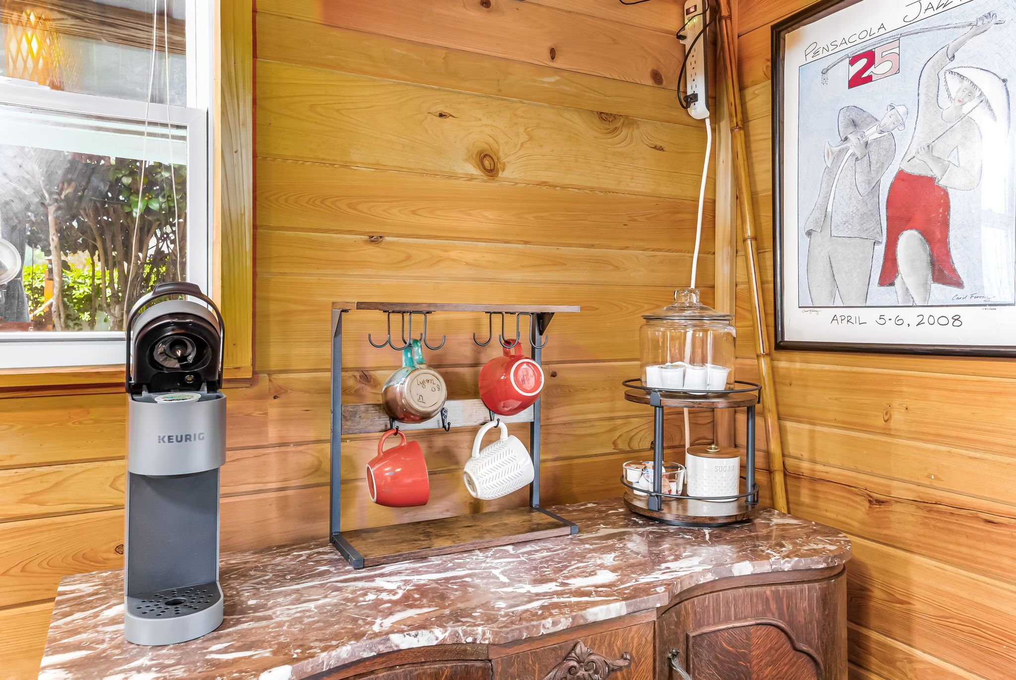 Eine Küchenzeile mit einer Keurig-Kaffeemaschine, einem Becherhalter und einem Zuckerbehälter auf einer Marmorarbeitsplatte.