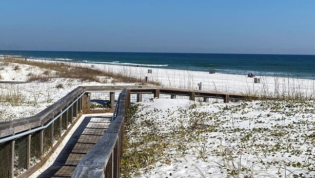 Ein Strand mit einem hölzernen Steg, der zum Ufer führt, Sanddünen und dem Meer.