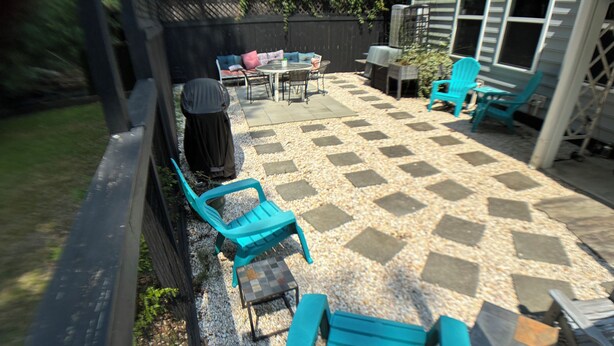 Un patio con piso de baldosas de cuadros, mobiliario exterior que incluye sillas y una mesa, y un área de estar cubierta.