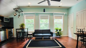 Sala de estar con un sofá negro, una mesa de comedor y una zona de cocina con microondas.