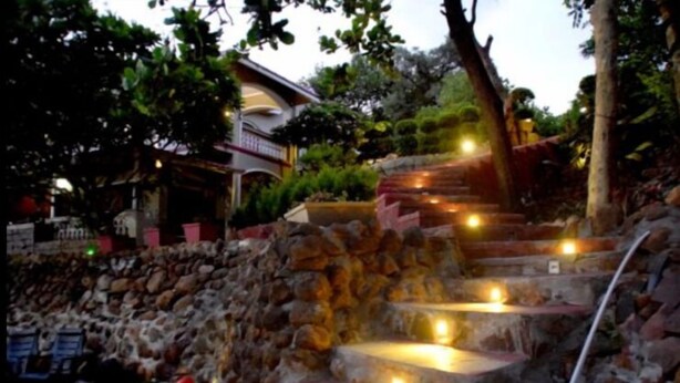 Un escalier en pierre dont les marches sont éclairées par des lampes, menant à un bâtiment doté d’un balcon.