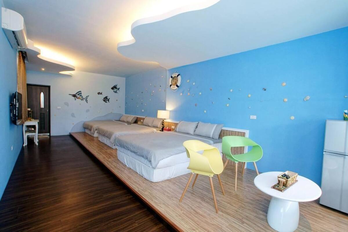 Une chambre moderne avec un grand lit, deux chaises, une petite table et un réfrigérateur.
