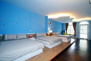 A hotel room with three beds, a wooden floor, a blue wall with climbing holds, a window with curtains, and a door. - Wei Feng Jia Yuan B&B (Taitung)
