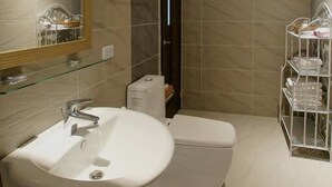 Une salle de bain moderne avec un grand miroir, un lavabo, des toilettes et une étagère en verre où sont rangés les articles de toilette.