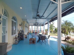 A covered outdoor area with tables and chairs, a ceiling fan, and a view of a swimming pool and palm trees. - Wei Feng Jia Yuan B&B (Taitung)
