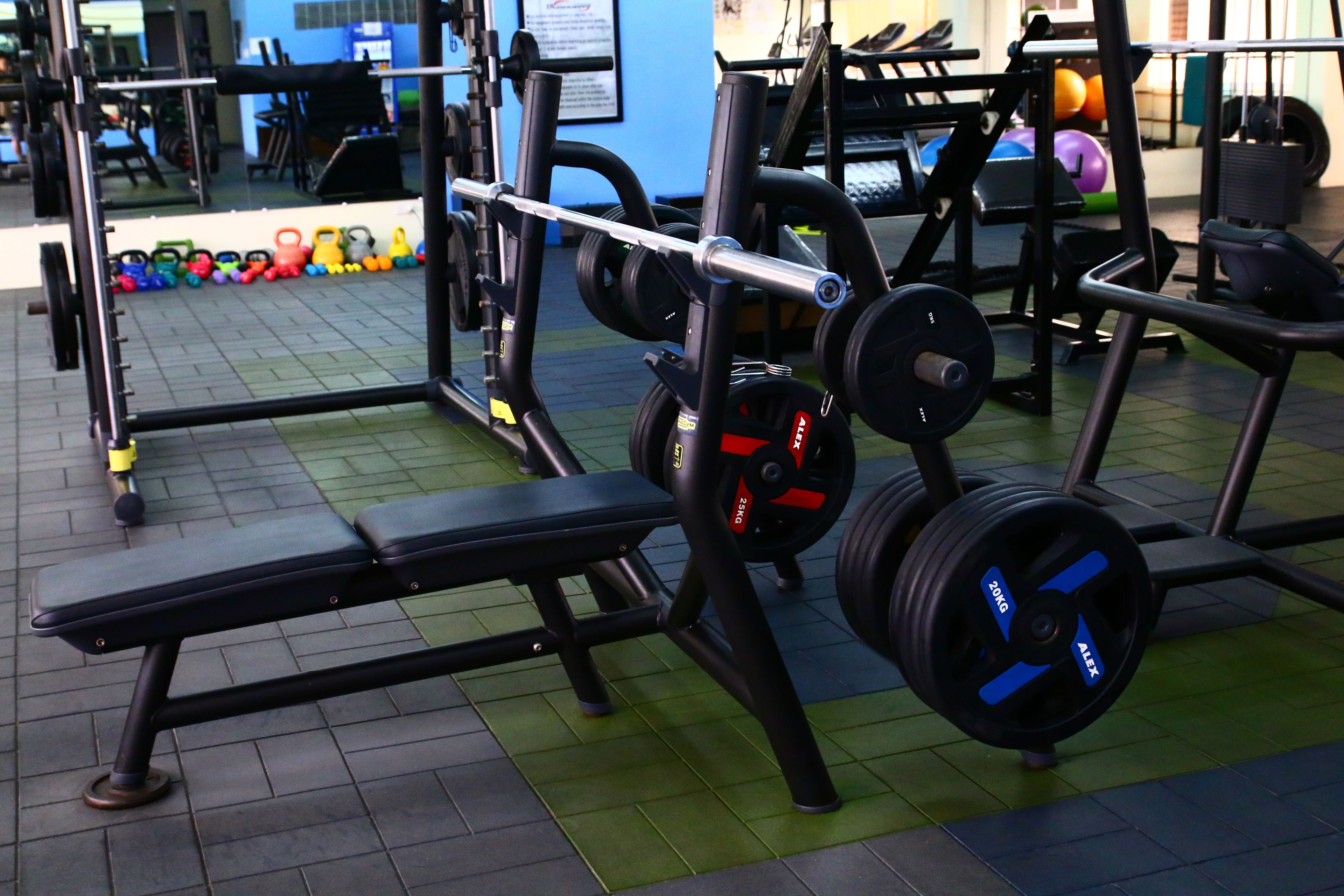 Een fitnessruimte met gewichthefapparatuur, een bank en een spiegel.