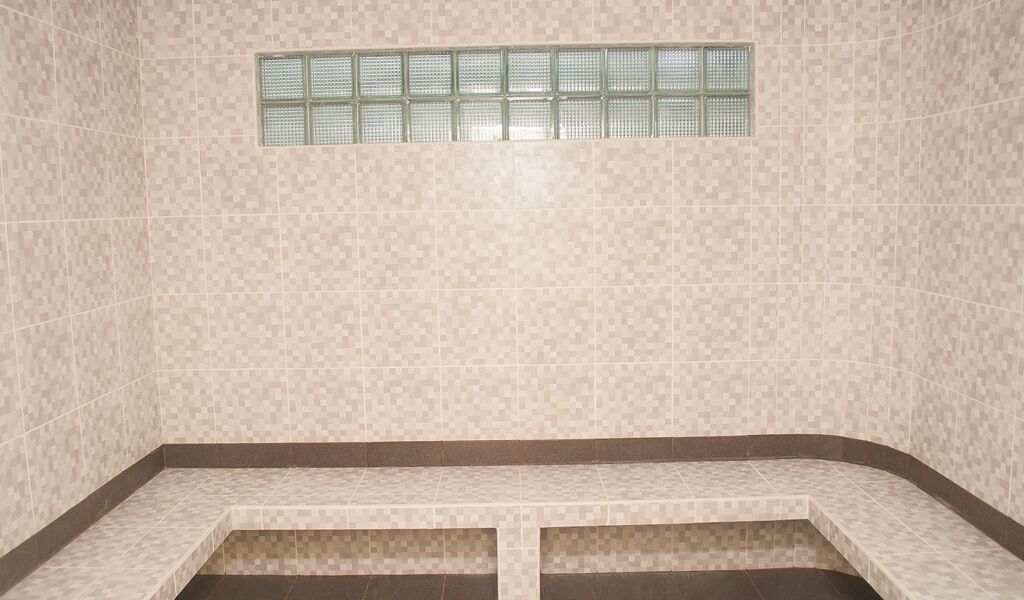 Casa de banho com paredes em azulejo, uma janela com padrão quadriculado e um banco.