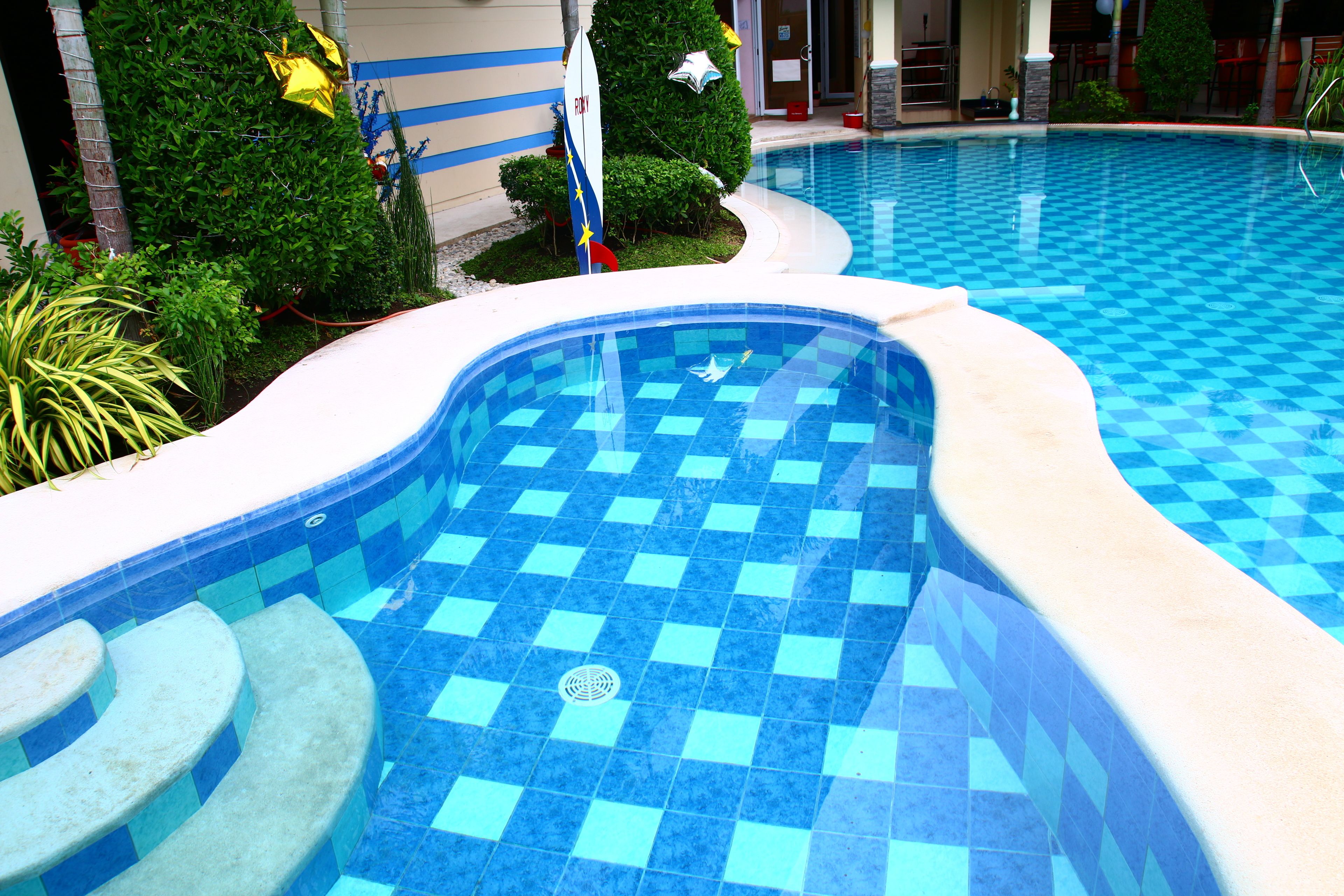 Una piscina con diseño de mosaico a cuadros, rodeada por un muro bajo y vegetación.