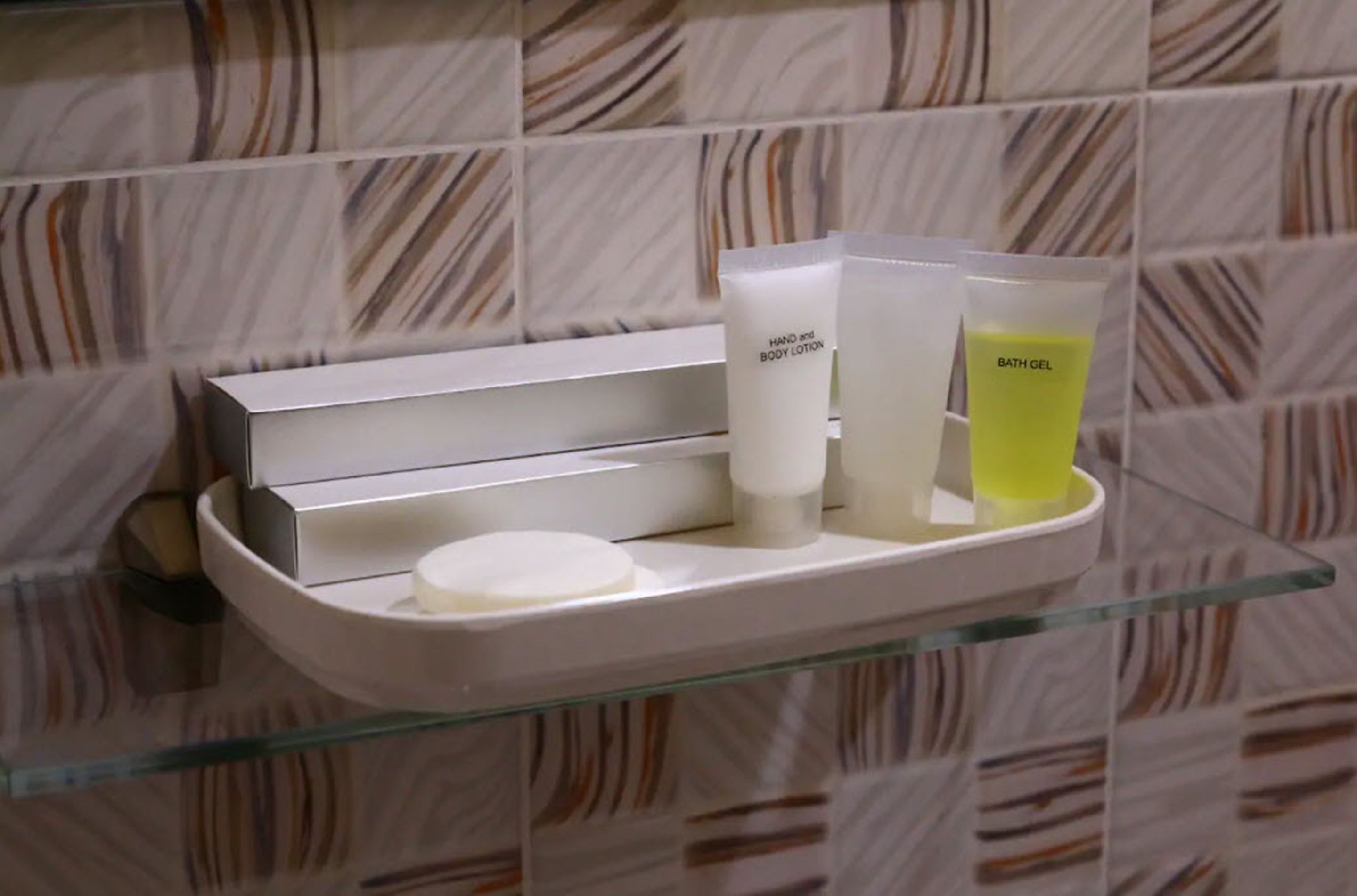 A bathroom shelf with toiletries including hand and body lotion, bath gel, and a soap bar.